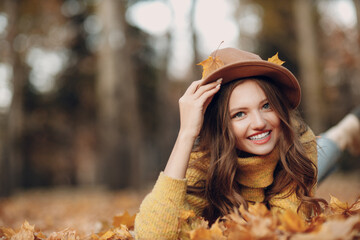 Young woman model lying in autumn park with yellow foliage maple leaves. Fall season fashion