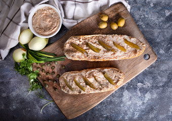 Sandwiches with rillettes, meat pate and pickled cucumber on a wooden cutting board, top view.
