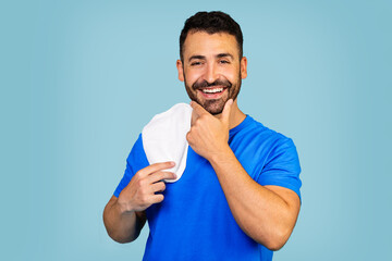  Photo of young happy man enjoying fresh perfectly smooth skin touching beard isolated on blue background