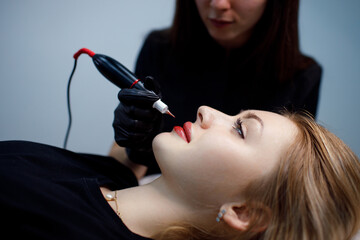 Applying procedure pink pigment permanent tattoo on female lips with tatooing needle machine - obrazy, fototapety, plakaty
