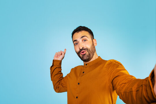 Excited European Man Showing Empty Space To The Side, Gesturing With His Hands, Standing Against A Blue Background.