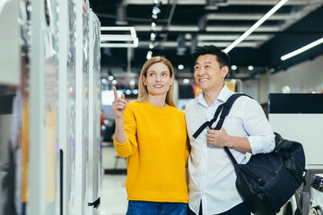 happy asian couple family man and woman make a choice choose of new household home appliances in supermarket survey Refrigerator Fridge cooler, freezer, cold store purchase and shopping