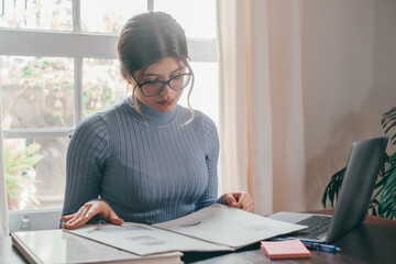 One young pretty woman studying and doing homework at home on the table. Female teenager using laptop or computer surfing the net indoor.