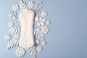 Women's sanitary napkins for the menstrual period decorated with white flowers and leaves on a blue...