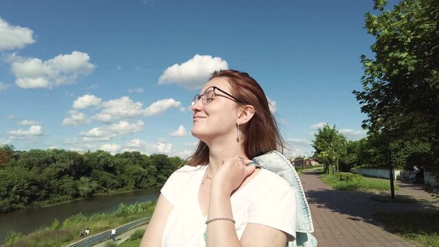 Carefree smiling young woman wearing eyeglasses and casual clothes enjoying a sunny summer day while breathing fresh air.