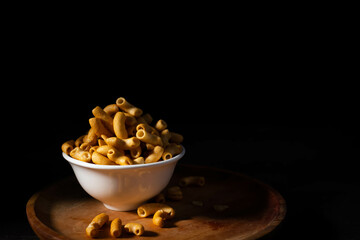 Macaroni snacks in bowl on dark background