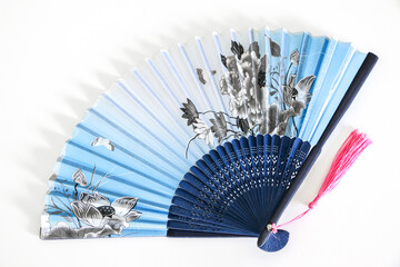 Blue Chinese oriental style fan (fengshan) with pink tassels on white background. Images of nature, butterflies over flowers on the fan. Useful for hot weather.