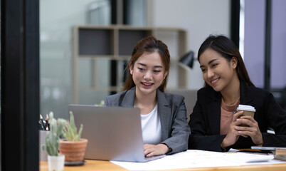 Two young Asian business woman talk, consult, discuss working with new startup project idea presentation analyze plan marketing and investment in the office.