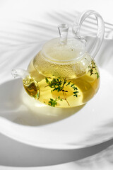 Yellow herbal tea with thyme in glass teapot. White background with copyspace.