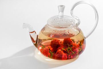 Red herbal berry tea with thyme and fresh raspberry in glass teapot. White background with copyspace.