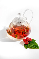 Red herbal berry tea with thyme and fresh raspberry in glass teapot. White background with copyspace.