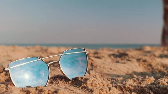 Sunglasses Lie On The Sand On The Beach, A Woman Is Walking Behind