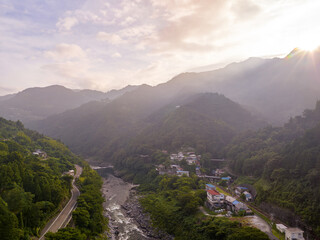 Early morning sun rays shine over mountain to small town by river in valley