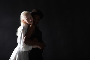 Caucasian albino girl and african american young woman hugging on black background. Women...