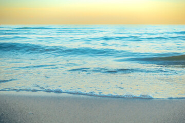 Serene and tranquil background of waves at the beach with a tropical yellow orange and gold sunset by the sea