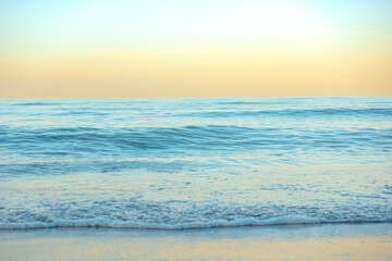 Serene and tranquil background of waves at the beach with a tropical yellow orange and gold sunset by the sea