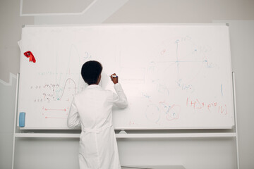 African American woman math teacher writing on whiteboard with marker.