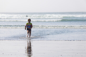 A child running out of the water onto a sandy beach with a reflective surface in Westport, Washington..