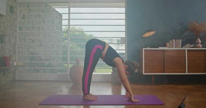Young woman learning yoga on a tablet. In a spacious room and overlooking the garden. Girl exercising at living room with online course