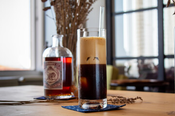 A long glass of black foamy coffee with a glasss coffee bottle on a wooden table. Concept