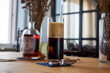 A long glass of black foamy coffee with a glasss coffee bottle on a wooden table. Concept
