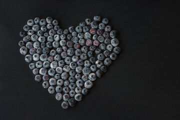 Heart made of frozen blueberries on the dark table, flat lay, horizontal background