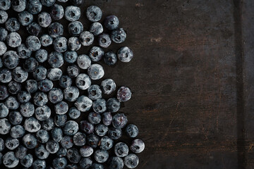 Frozen blueberry covering a left half of an old scratched metal baking sheet horizontal background