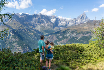 Rear view of a standing couple with their toddler enjoying Matterhorn views during a summer hiking day at Italian Alps. Family active vacations.