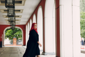 European plus size woman walking outdoor street city. Young red pink haired body positive girl.