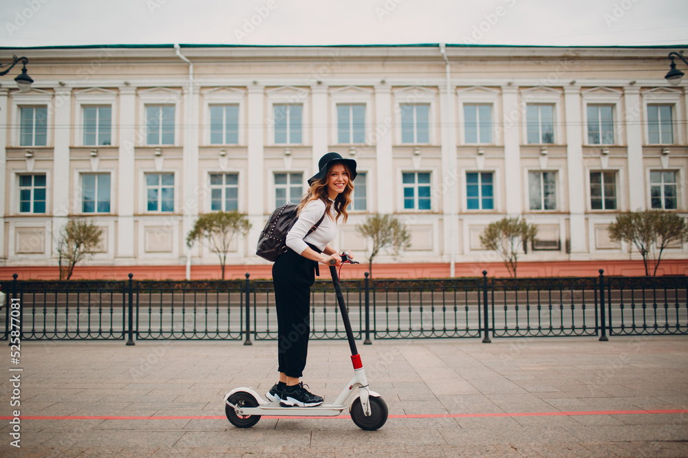 Wall mural Young woman with electric scooter at the city.