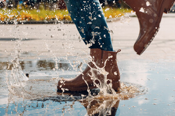 Woman wearing rain rubber boots walking running and jumping into puddle with water splash and drops...