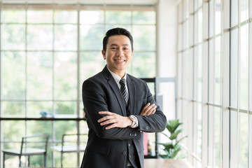 Portrait of happy mature Asian business man standing with arms crossed at the office work