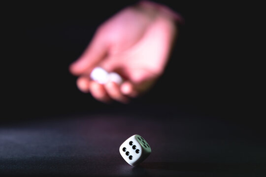 Dados blancos rodados por la mano de una mujer sobre fondo negro &ndash; enfoque selectivo.