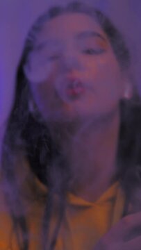 The girl smokes a vape releases a lot of steam. Color light. Vertical video