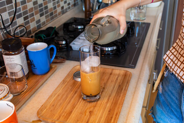 A woman hand preparing a glass of cold coffee on a wooden cutting board at kitchen