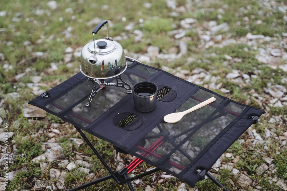 Poster Camping furniture folding table made of netting, camping utensils, a glass of tea, a metal kettle stands on a gas burner.