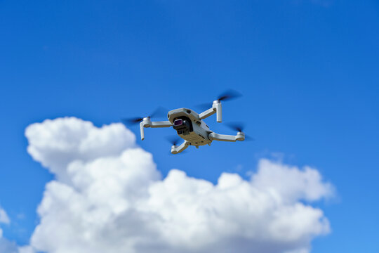 Gray quadcopter with a camera in vivid blue sky white clouds