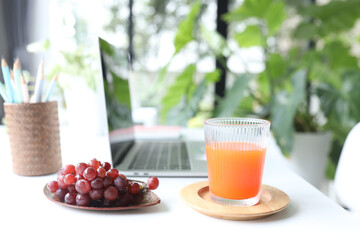 Orange in a glass cup and grapes and laptop indoor work from home