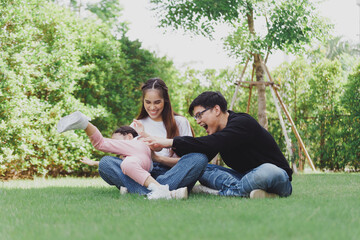 Asian Family with a child playing on a lawn, Family sitting on the grass with her happy and adorable little daughter, enjoyment relaxing recreational concept.