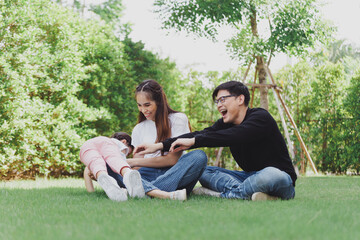 Naklejka premium Asian Family with a child playing on a lawn, Family sitting on the grass with her happy and adorable little daughter, enjoyment relaxing recreational concept.