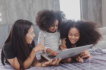 Asian family portrait at home, family enjoying leisure time, Family lying on bed using their laptop at home, Happy family lies on bed and watching something on laptop.