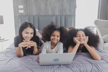 Asian family portrait at home, family enjoying leisure time, Family lying on bed using their laptop at home, Happy family lies on bed and watching something on laptop.