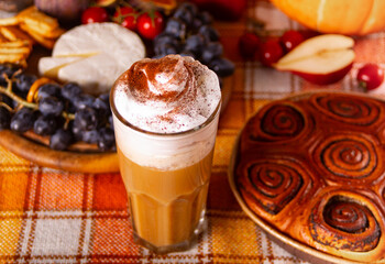 Pumpkin spice whipped latte in glass. Hot autumn drink beverage. Nearby delicious pie and appetizers fruits and cheese.