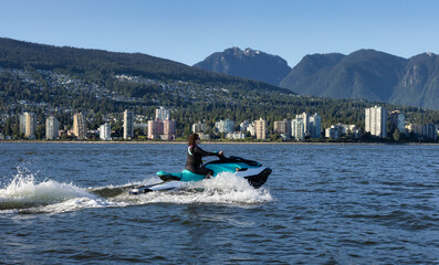 Fototapeta premium Adventurous Caucasian Woman on Water Scooter riding in the Ocean. Modern City and mountains in background. North Vancouver, British Columbia, Canada.