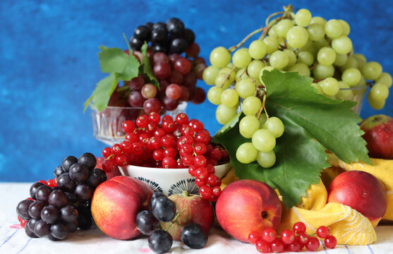 Colorful still life with seasonal berries on a table. Red currant, green grapes, nectarines and apples close up photo. Nutrition concept. 