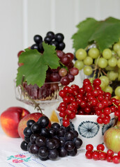 Colorful still life with seasonal berries on a table. Red currant, green grapes, nectarines and apples close up photo. Nutrition concept. 