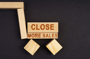 On a black surface, a cart made of blocks and cubes with the inscription - Close More Sales
