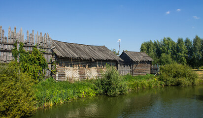 The ancient Shchurovskoye settlement in Suzdal in Russia with medieval wooden buildings among the bright green foliage of trees on the shore of a pond with a reflection on a sunny summer day