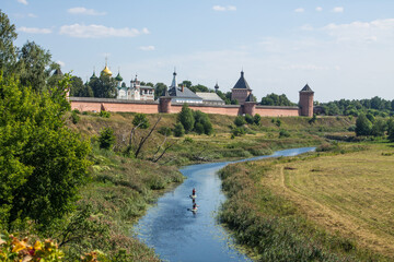 Panoramic view of the old brick walls of the Suzdal Kremlin on a high hill on the banks of the beautiful Kamenka river among the green grass on a sunny summer day in Russia