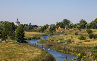 Tourists are rafting on the winding Kamenka river in Suzdal Russia among meadows with grass on a sunny summer bright day and a space for copying